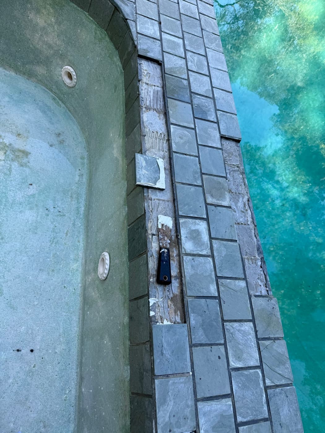 Damaged pool coping tiles with deteriorated grout before professional pool tile repair service
